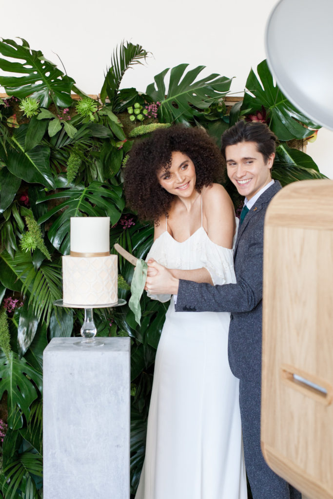 Bride and groom cutting wedding cake with photo booth