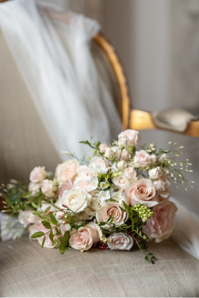 Wedding veil displayed on chair with blush and pink bouquet