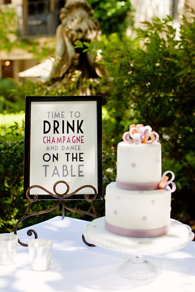 2 tier fondant wedding cake with polka dots displayed next to framed sign