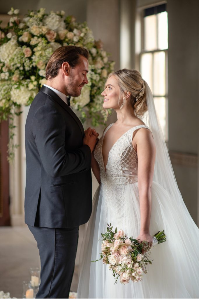 Bride and groom standing together in front of flower arrangement