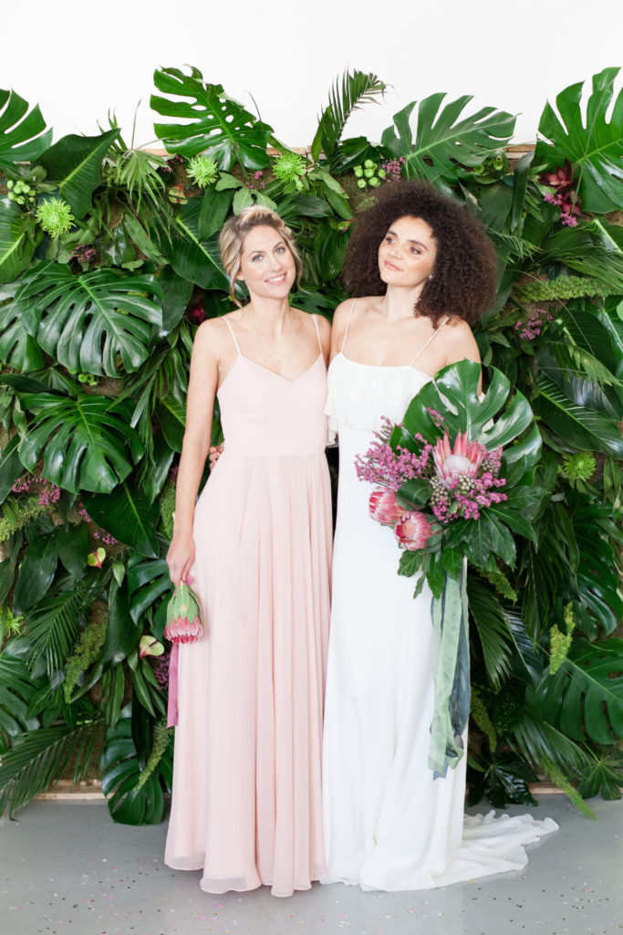 Bridesmaid and bride standing in front of greenery wall