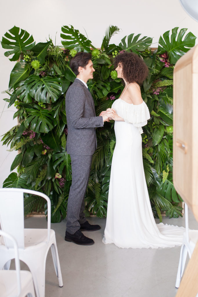 Bride and groom standing in front of greenery wall