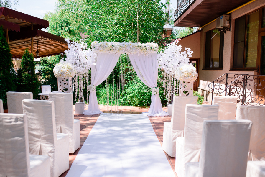 Outdoor wedding ceremony with draped canopy, large floral displays and chairs lining the aisle