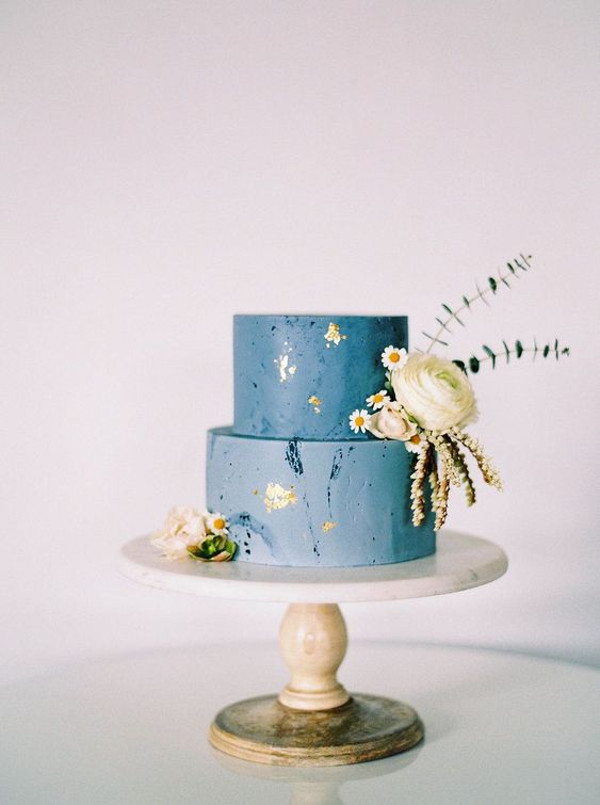 a two-tier blue wedding cake with gold detail and white flowers
