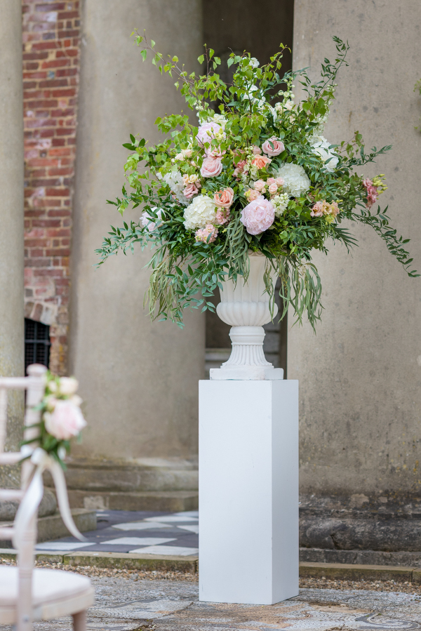 foam free flowers in blush pink and greenery in a stone urn on white plinth 
