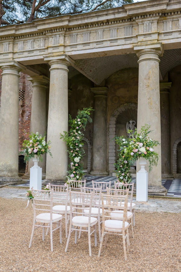 Outdoor wedding ceremony with asymmetrical arch and pillar flower arrangements