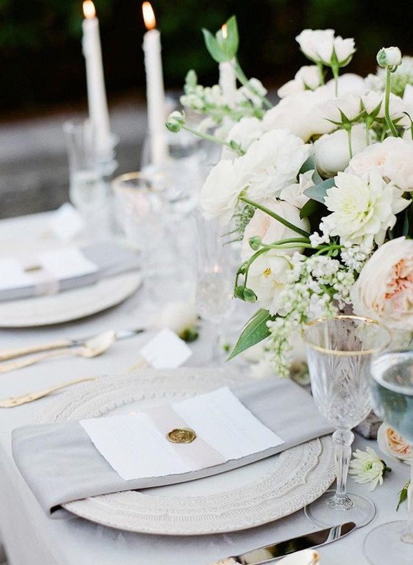 Wedding table set with glasses with gold rims, grey napkins, blush and cream flowers and candles