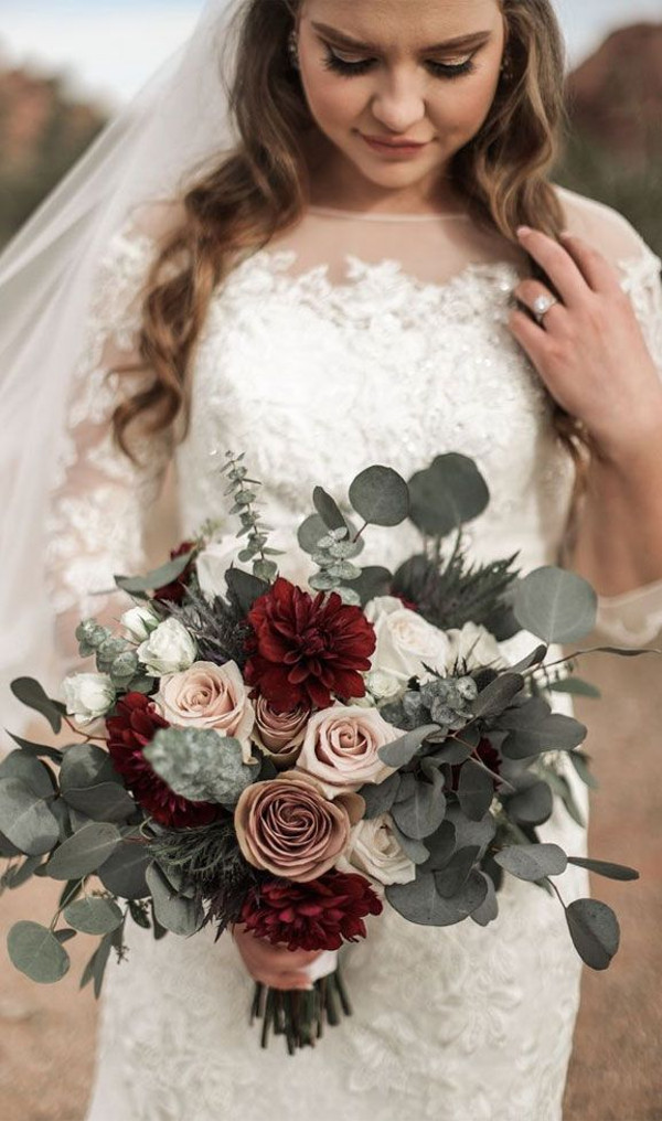 Bride in white lace wedding dress with a bouquet in shades of blush, burgundy, deep red and greenery