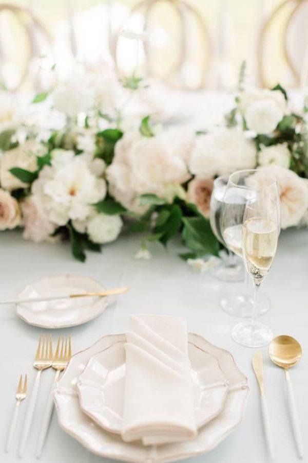 wedding table set up with white handled cutlery and gold rimmed white plates, floral centrepiece with white peonies and greenery