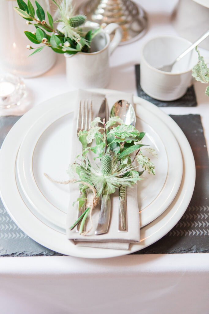Place setting withite places and silver cutlery tied with greenery