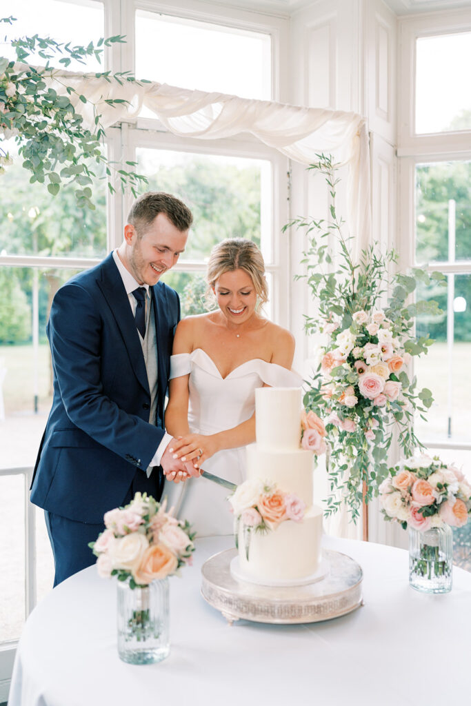 Bride and groom cutting 3 tier wedding cake at Morden Hall