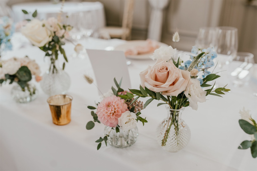 Bud vases in pastel colours on wedding table with god tea light holders