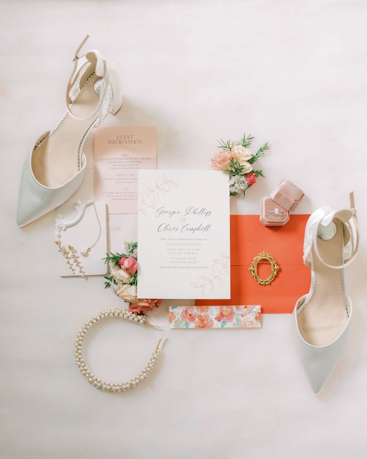 Coral wedding flat lay with invitation, wedding shoes and jewellery